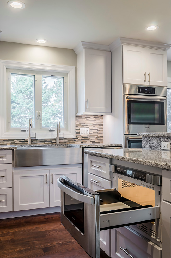 Inspiration for a mid-sized transitional u-shaped medium tone wood floor eat-in kitchen remodel in Chicago with a farmhouse sink, recessed-panel cabinets, white cabinets, granite countertops, gray backsplash, glass tile backsplash, stainless steel appliances and an island