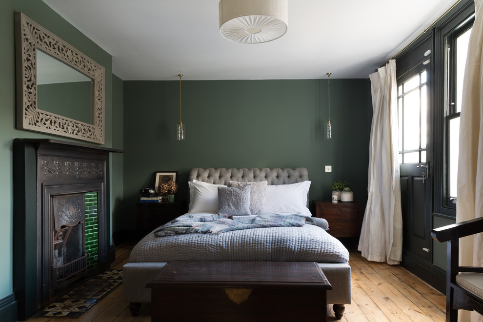 Transitional master bedroom in London with green walls, light hardwood floors and a standard fireplace.