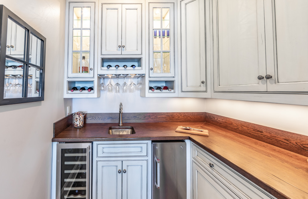 This is an example of a mid-sized transitional l-shaped wet bar in Charlotte with an undermount sink, recessed-panel cabinets, beige cabinets, wood benchtops, medium hardwood floors, brown floor and brown benchtop.