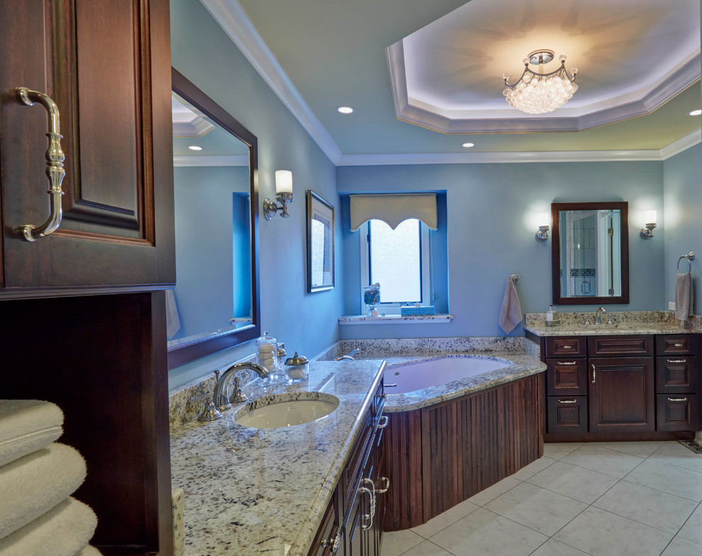 Large transitional master ceramic tile and beige floor bathroom photo in Chicago with raised-panel cabinets, dark wood cabinets, an undermount tub, blue walls, an undermount sink and granite countertops