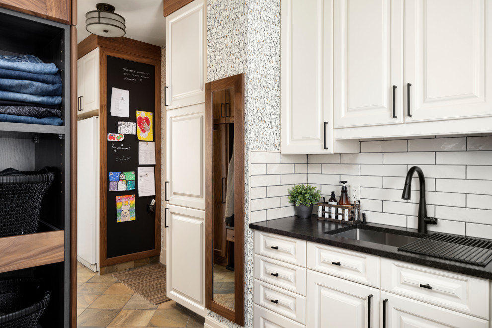 カルガリーにある高級な広いトランジショナルスタイルのおしゃれな家事室 (L型、アンダーカウンターシンク、落し込みパネル扉のキャビネット、中間色木目調キャビネット、御影石カウンター、白いキッチンパネル、サブウェイタイルのキッチンパネル、スレートの床、茶色い床、黒いキッチンカウンター、壁紙、ベージュの壁) の写真