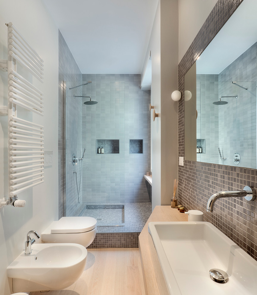 Inspiration for a contemporary bathroom in Rome with an open shower, a wall-mount toilet, black tile, gray tile, white walls, light hardwood floors, a trough sink, wood benchtops, an open shower and beige benchtops.