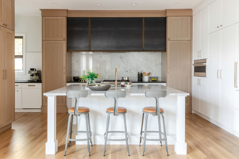Design ideas for a mid-sized transitional u-shaped eat-in kitchen in Calgary with recessed-panel cabinets, light wood cabinets, marble benchtops, white splashback, marble splashback, white appliances, medium hardwood floors, with island, brown floor, white benchtop and exposed beam.