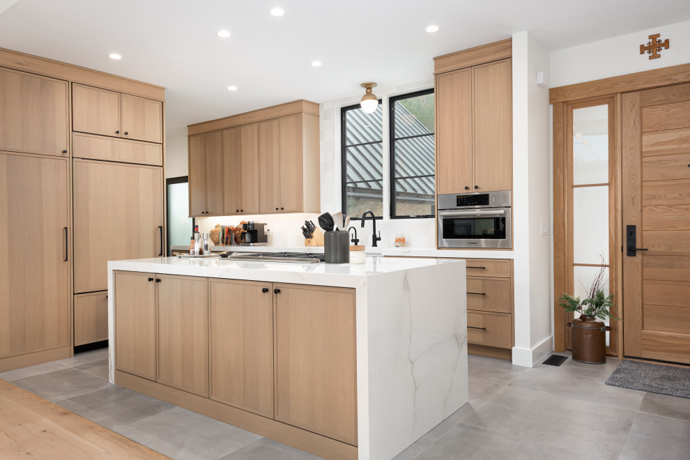 Mid-sized transitional l-shaped kitchen in Other with a farmhouse sink, shaker cabinets, light wood cabinets, white splashback, ceramic splashback, panelled appliances, cement tiles, with island, grey floor and white benchtop.