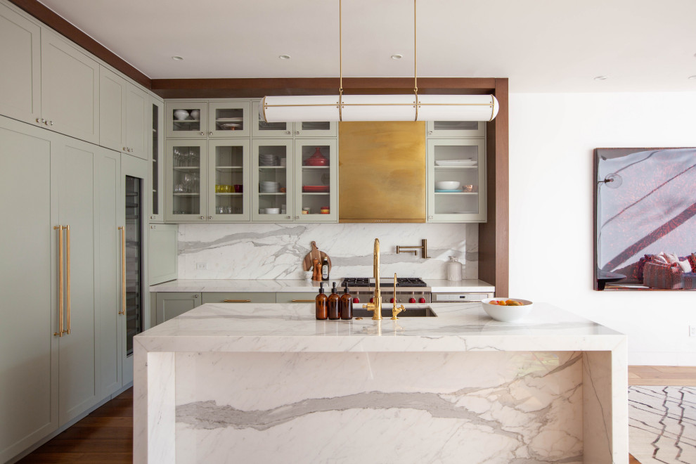 This is an example of a large contemporary u-shaped open plan kitchen in New York with an integrated sink, shaker cabinets, green cabinets, marble benchtops, white splashback, marble splashback, stainless steel appliances, medium hardwood floors, with island, brown floor and white benchtop.