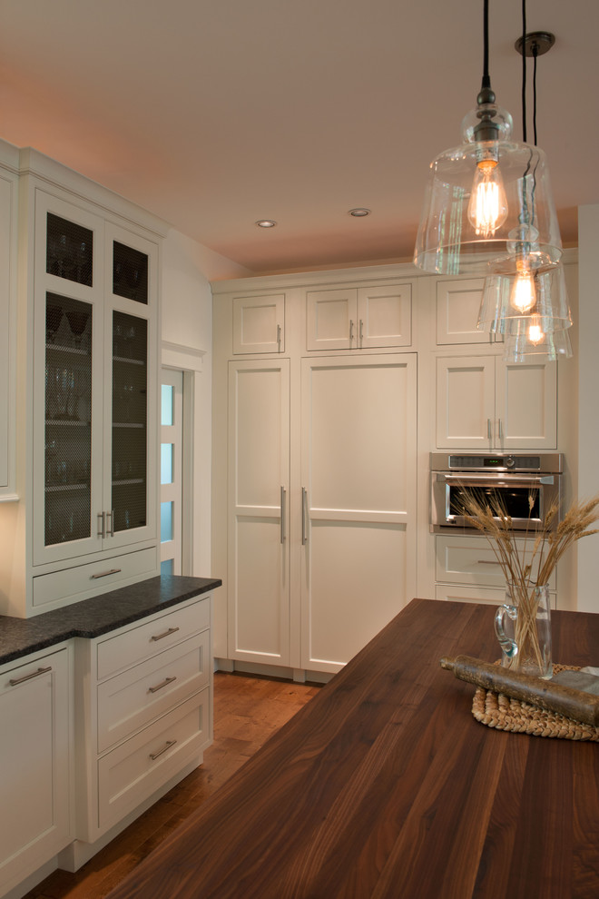 Eat-in kitchen - mid-sized transitional l-shaped eat-in kitchen idea in Boston with recessed-panel cabinets, wood countertops and paneled appliances