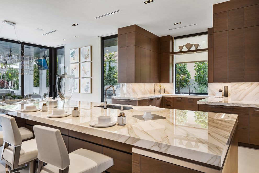 Photo of a large modern kitchen in Miami with a drop-in sink, flat-panel cabinets, medium wood cabinets, onyx benchtops, beige splashback, marble floors, with island, white floor and beige benchtop.
