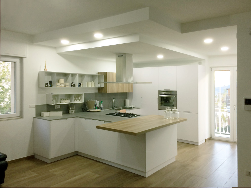This is an example of a mid-sized contemporary u-shaped open plan kitchen with an integrated sink, flat-panel cabinets, white cabinets, marble benchtops, marble splashback, stainless steel appliances, porcelain floors, a peninsula and grey splashback.