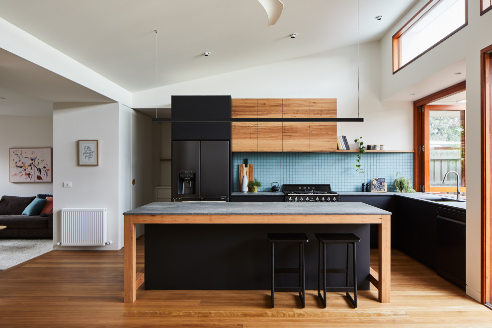 Photo of a contemporary l-shaped kitchen in Melbourne with an undermount sink, flat-panel cabinets, black cabinets, blue splashback, mosaic tile splashback, black appliances, medium hardwood floors, with island, brown floor, grey benchtop and vaulted.