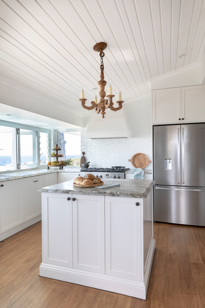 Mid-sized tropical u-shaped kitchen pantry in Brisbane with an undermount sink, shaker cabinets, white cabinets, granite benchtops, white splashback, ceramic splashback, stainless steel appliances, medium hardwood floors, with island and multi-coloured benchtop.