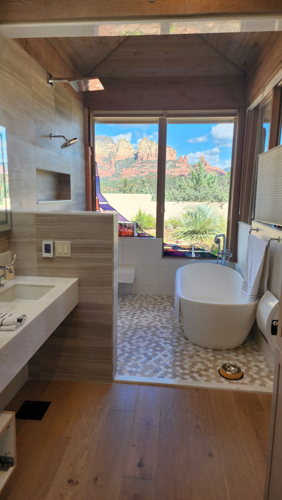This is an example of a large coastal ensuite bathroom in Phoenix with white cabinets, a freestanding bath, a built-in shower, brown tiles, stone tiles, white walls, light hardwood flooring, a submerged sink, marble worktops, brown floors, an open shower, white worktops, a shower bench, double sinks, a floating vanity unit and a vaulted ceiling.