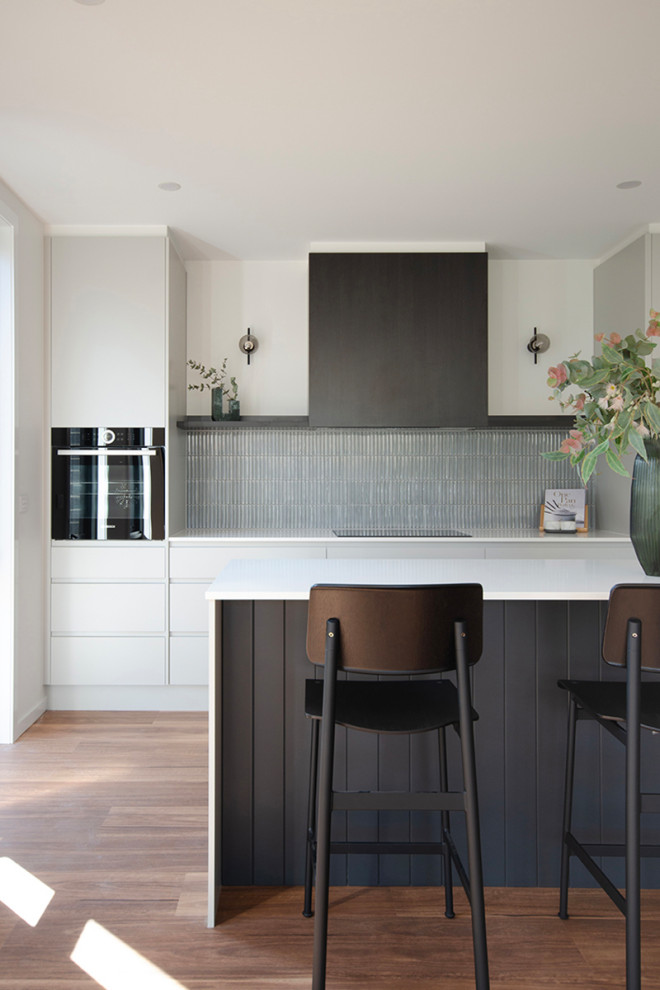 Esempio di una cucina minimalista di medie dimensioni con lavello sottopiano, ante grigie, top in quarzo composito, paraspruzzi grigio, paraspruzzi con piastrelle a mosaico, elettrodomestici neri, pavimento in vinile, pavimento marrone e top bianco