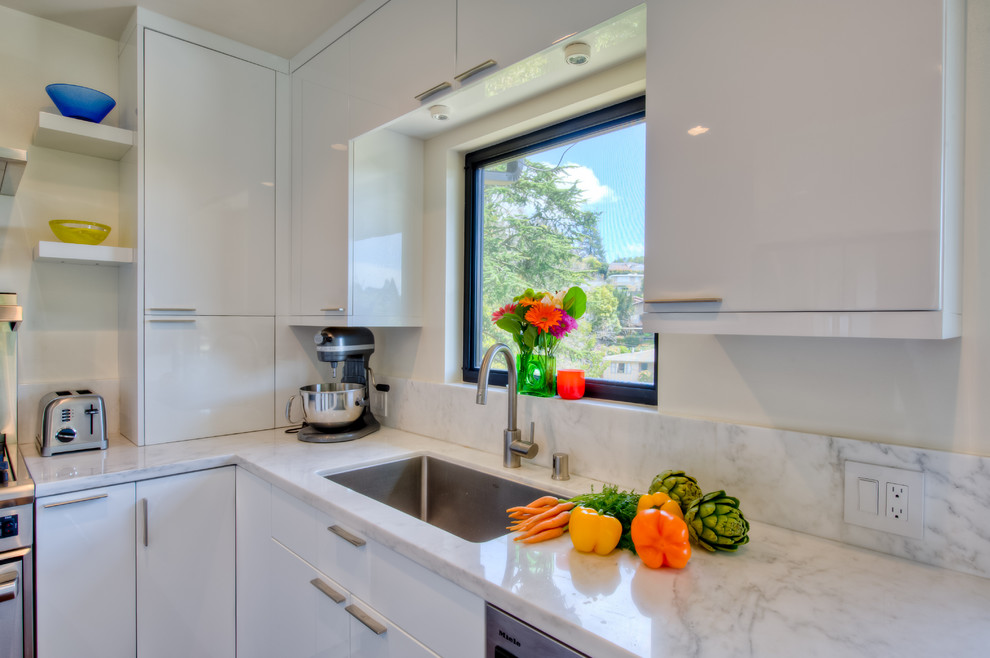 This is an example of a small contemporary u-shaped open plan kitchen in San Francisco with an undermount sink, flat-panel cabinets, white cabinets, marble benchtops, white splashback, subway tile splashback, stainless steel appliances, medium hardwood floors, no island and beige floor.