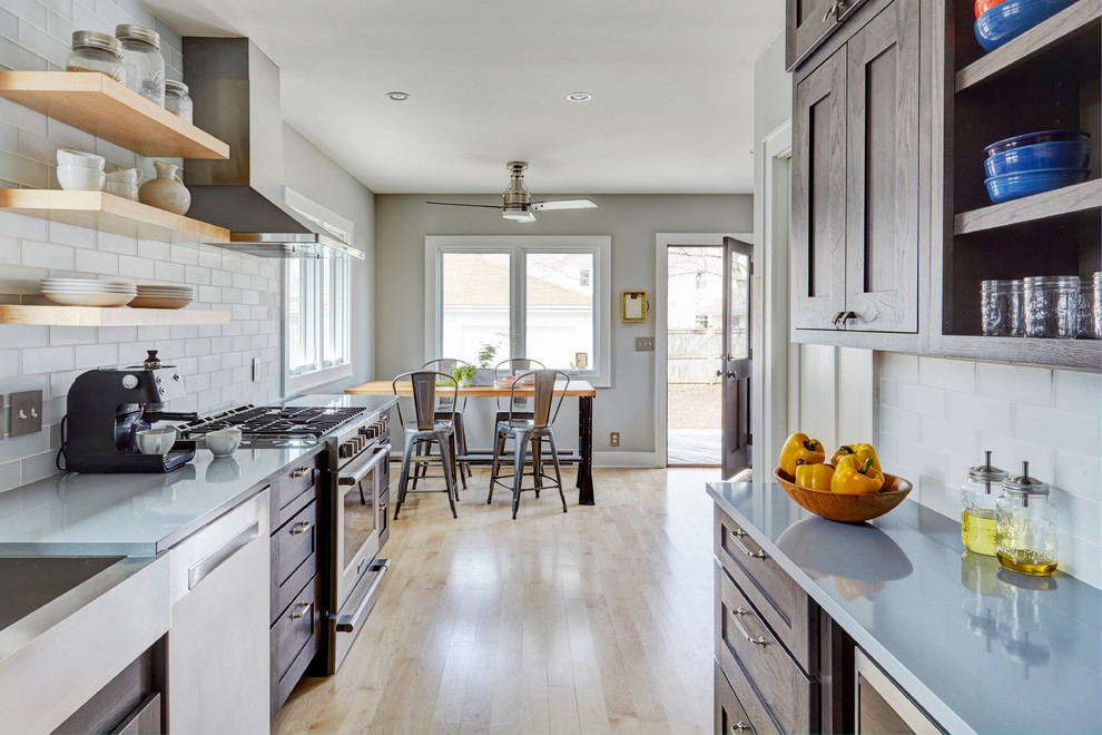 This is an example of a mid-sized transitional galley eat-in kitchen in Milwaukee with a farmhouse sink, flat-panel cabinets, dark wood cabinets, quartzite benchtops, white splashback, glass tile splashback, stainless steel appliances, light hardwood floors, no island, beige floor and grey benchtop.