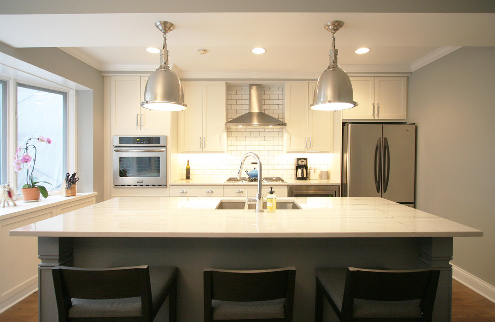 Inspiration for a large transitional medium tone wood floor kitchen remodel in Chicago with an undermount sink, shaker cabinets, white cabinets, quartzite countertops, white backsplash, subway tile backsplash, stainless steel appliances and an island