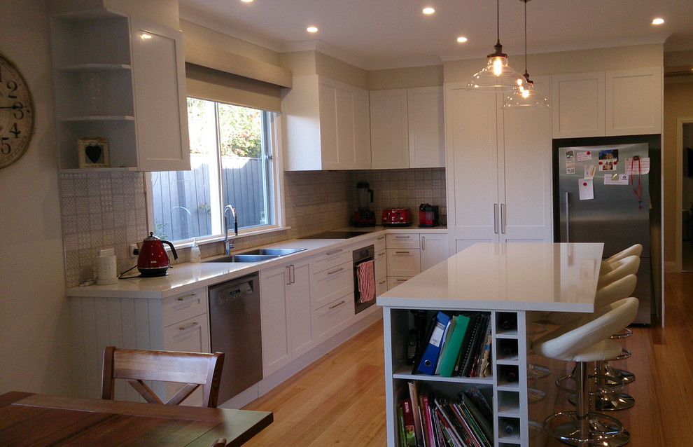 This is an example of a large contemporary l-shaped open plan kitchen in Melbourne with shaker cabinets, white cabinets, quartz benchtops, with island, a drop-in sink, beige splashback, porcelain splashback, black appliances and medium hardwood floors.