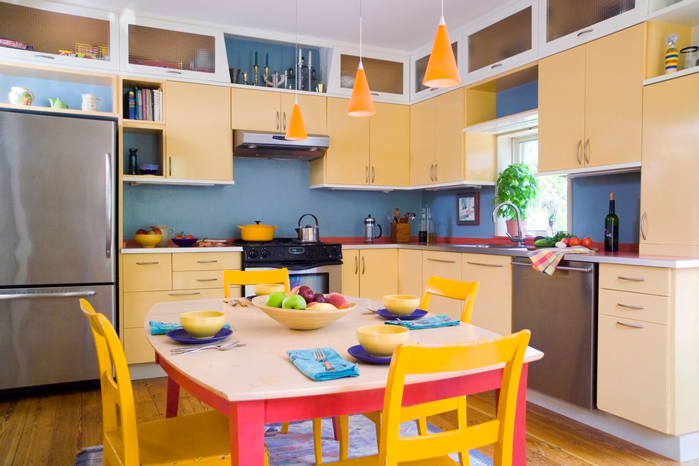 Design ideas for a mid-sized eclectic l-shaped eat-in kitchen in Boston with stainless steel appliances, yellow cabinets, an undermount sink, flat-panel cabinets, solid surface benchtops, medium hardwood floors and no island.