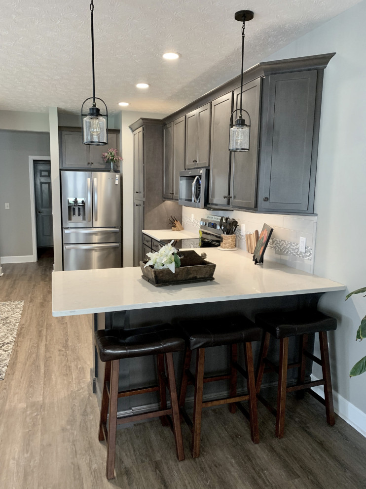 Inspiration for a large transitional u-shaped vinyl floor and gray floor open concept kitchen remodel with an undermount sink, shaker cabinets, gray cabinets, quartz countertops, gray backsplash, ceramic backsplash, stainless steel appliances, a peninsula and white countertops
