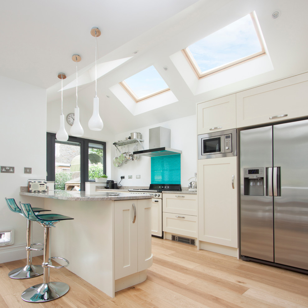 Design ideas for a transitional galley open plan kitchen in Other with shaker cabinets, white cabinets, blue splashback, glass tile splashback, stainless steel appliances, light hardwood floors and a peninsula.