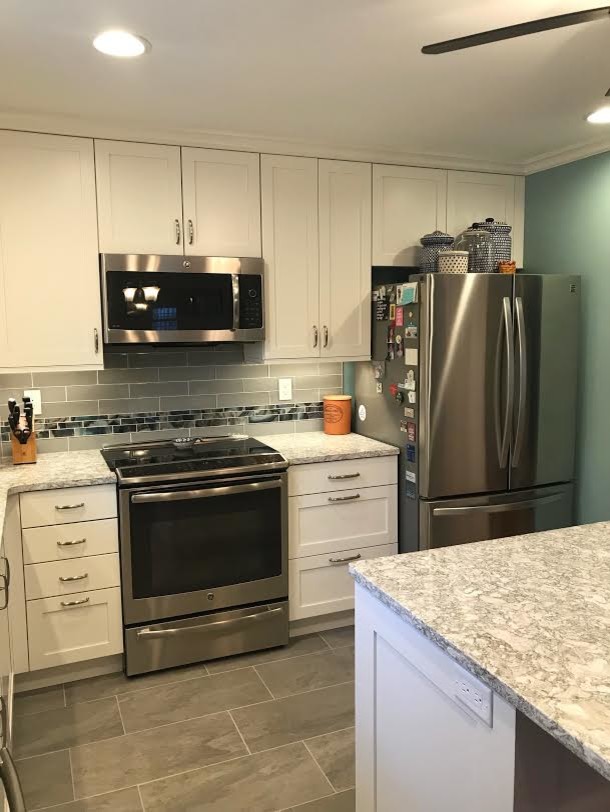 Photo of a mid-sized transitional l-shaped eat-in kitchen in Baltimore with an undermount sink, shaker cabinets, white cabinets, quartz benchtops, grey splashback, glass tile splashback, stainless steel appliances, porcelain floors, with island and grey floor.