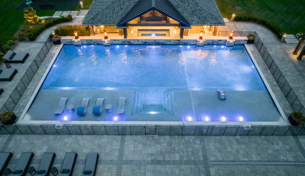 Modelo de piscina clásica renovada extra grande rectangular en patio trasero con paisajismo de piscina y adoquines de hormigón