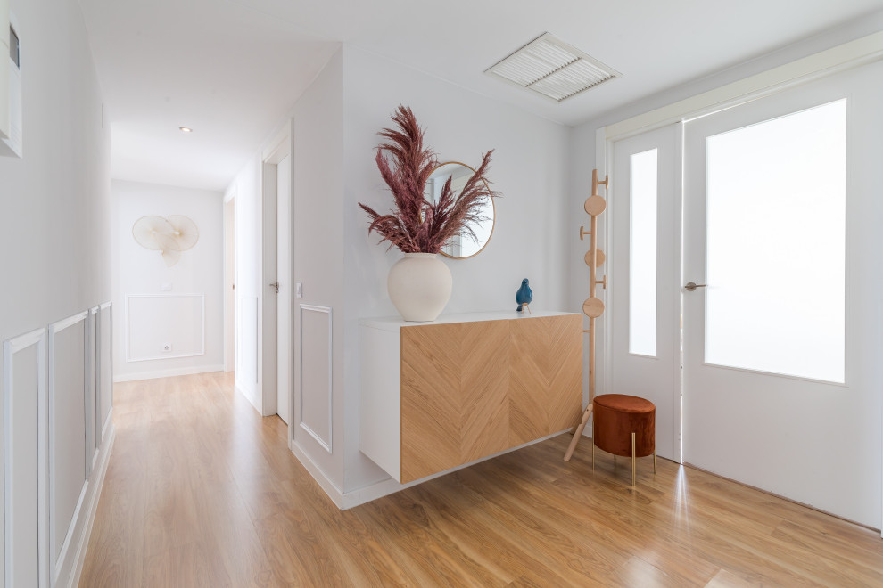 This is an example of a medium sized classic hallway in Madrid with white walls, medium hardwood flooring, a single front door and panelled walls.