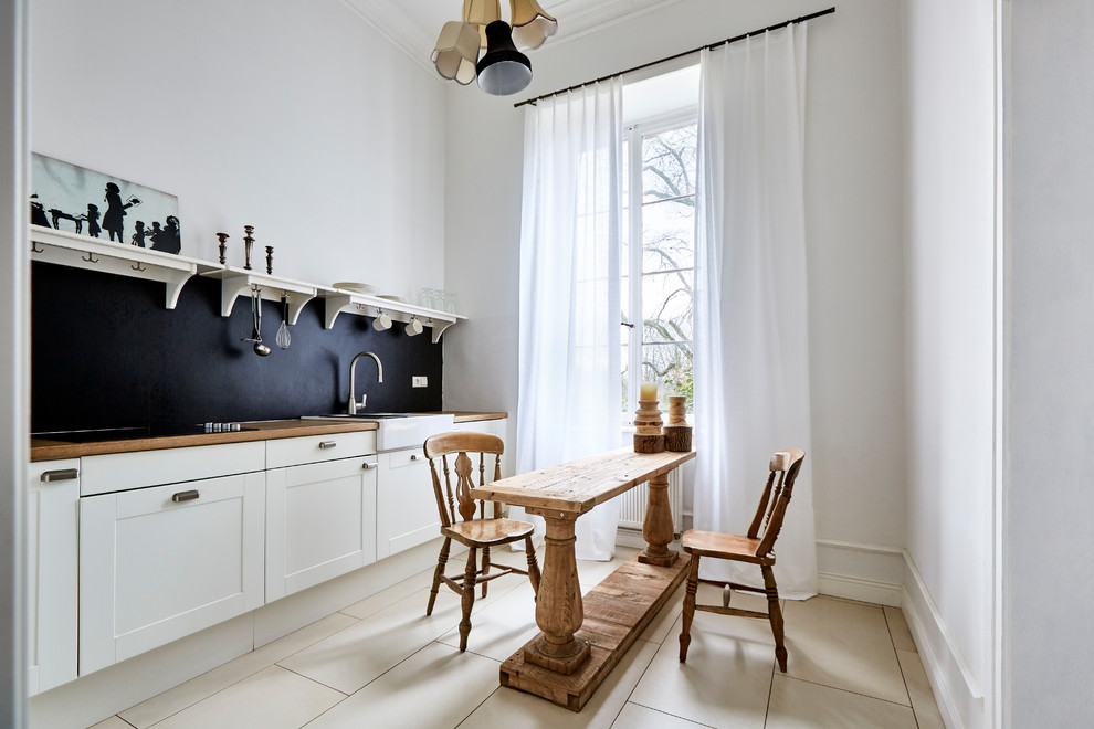 This is an example of a small traditional single-wall open plan kitchen in Frankfurt with an integrated sink, beaded inset cabinets, white cabinets, wood benchtops, black splashback, porcelain floors, beige floor and no island.