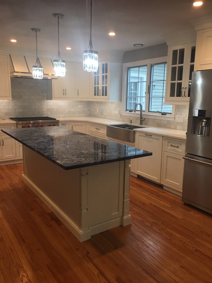 Inspiration for a mid-sized transitional l-shaped medium tone wood floor and brown floor kitchen remodel in Boston with a farmhouse sink, shaker cabinets, white cabinets, granite countertops, gray backsplash, subway tile backsplash, stainless steel appliances and an island