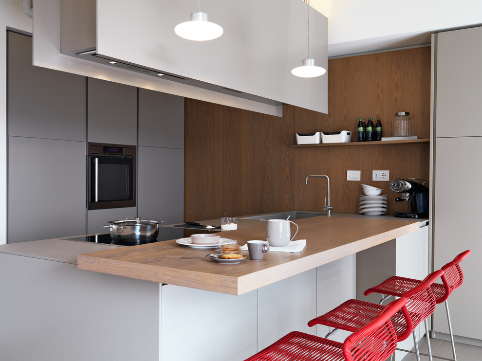 Photo of a contemporary galley kitchen in Milan with an integrated sink, flat-panel cabinets, grey cabinets, wood benchtops, stainless steel appliances, a peninsula, brown benchtop, brown splashback and window splashback.