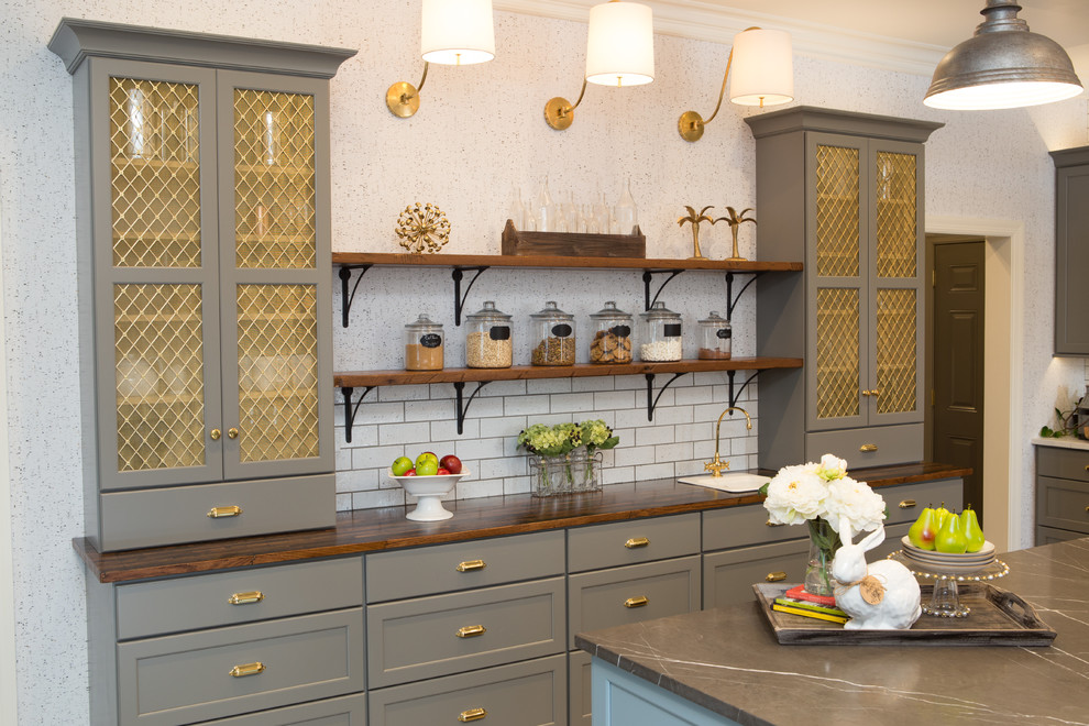 Inspiration for a large transitional u-shaped eat-in kitchen in Chicago with a farmhouse sink, shaker cabinets, grey cabinets, limestone benchtops, white splashback, subway tile splashback, black appliances, porcelain floors, with island and grey floor.
