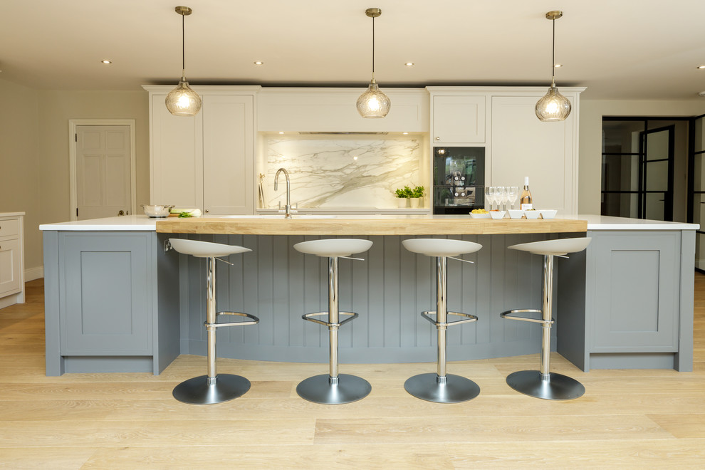 This is an example of a transitional galley kitchen in Berkshire with shaker cabinets, white cabinets, multi-coloured splashback, light hardwood floors, with island, beige floor and white benchtop.