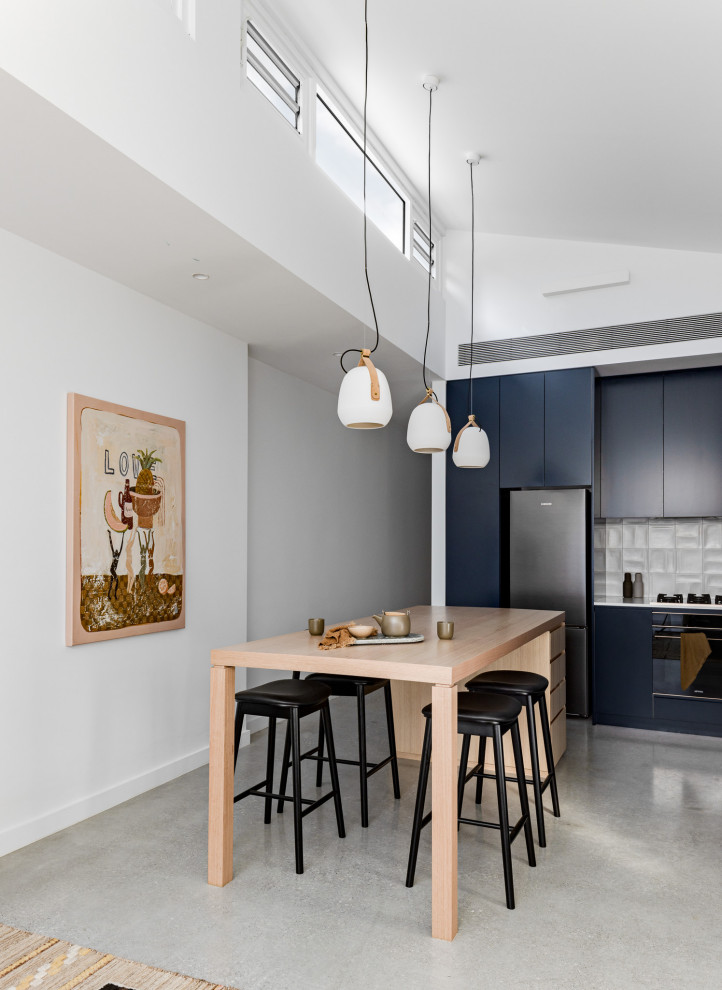 Photo of a small contemporary l-shaped kitchen/diner in Sydney with a submerged sink, blue cabinets, engineered stone countertops, white splashback, ceramic splashback, black appliances, concrete flooring, an island, grey floors and white worktops.