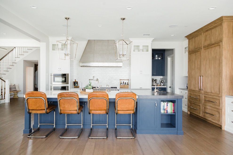 Inspiration for a beach style l-shaped kitchen in San Diego with shaker cabinets, blue cabinets, white splashback, subway tile splashback, light hardwood floors, with island, brown floor and white benchtop.