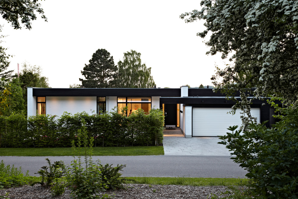 Photo of a large contemporary split-level white house exterior in Copenhagen with painted brick siding, a flat roof and a black roof.