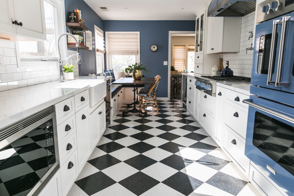 Inspiration for a mid-sized eclectic galley eat-in kitchen in San Francisco with a farmhouse sink, shaker cabinets, white cabinets, quartz benchtops, white splashback, ceramic splashback, coloured appliances, vinyl floors, no island, black floor and white benchtop.