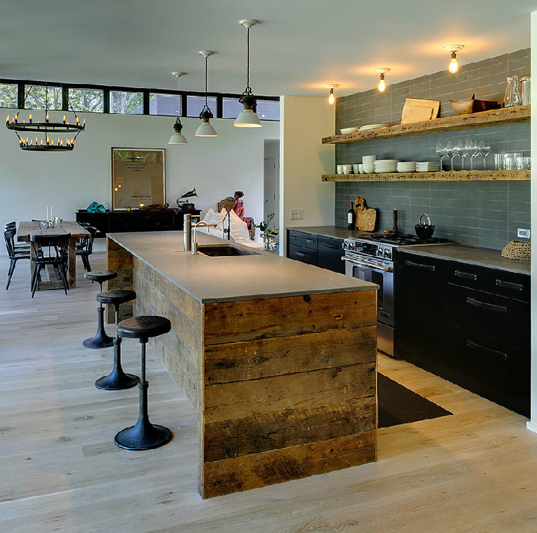 This is an example of a country open plan kitchen in San Diego with flat-panel cabinets, black cabinets, soapstone benchtops, grey splashback, cement tile splashback, light hardwood floors and with island.