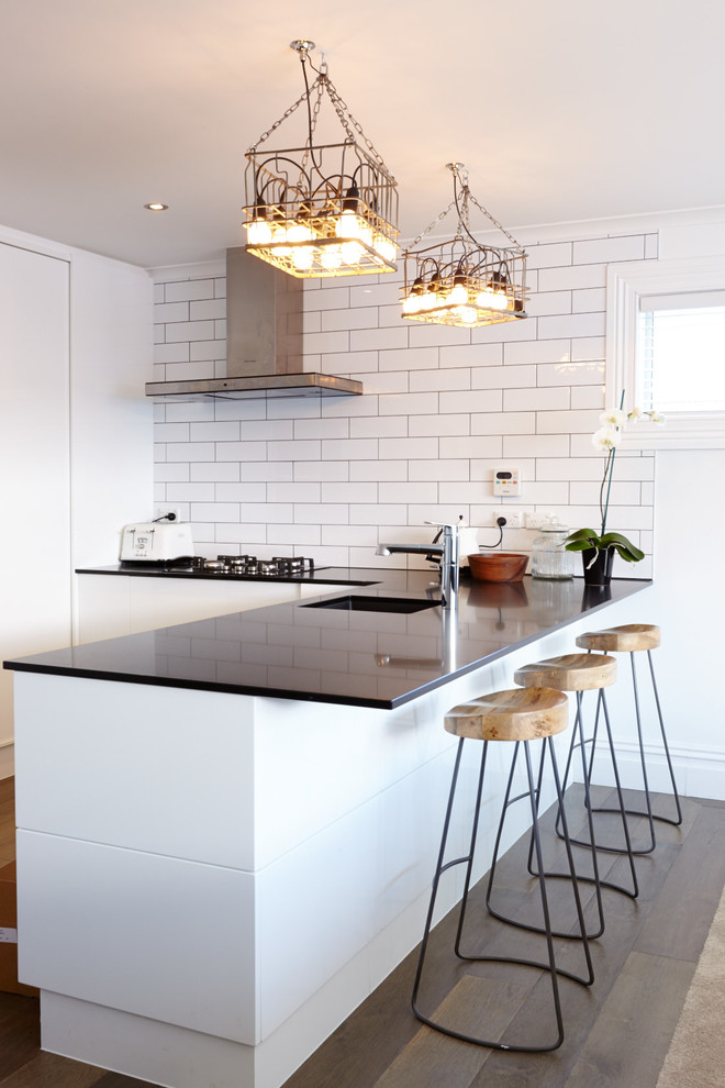 Photo of a small contemporary kitchen in Auckland with flat-panel cabinets, white cabinets, white splashback, subway tile splashback and a peninsula.