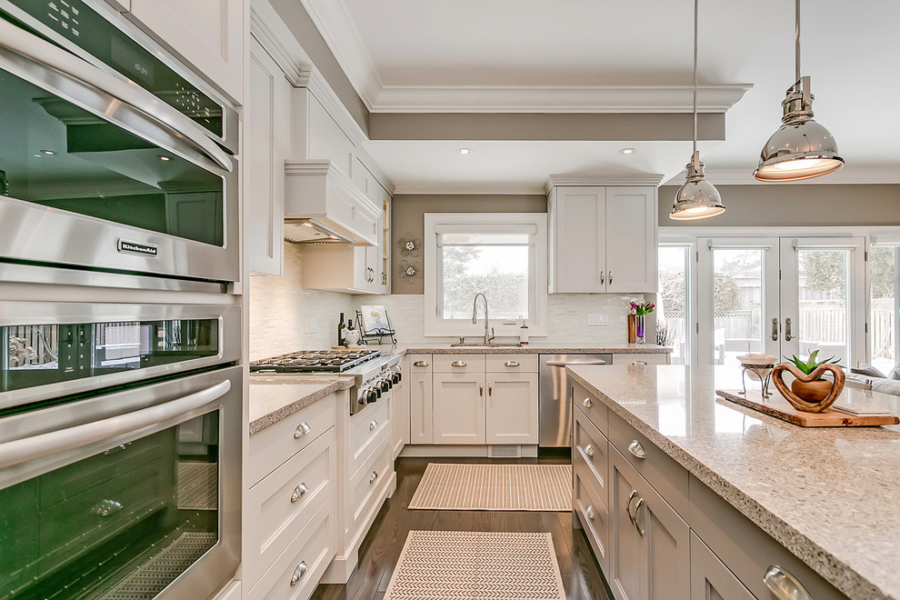 Example of a mid-sized transitional l-shaped medium tone wood floor and brown floor open concept kitchen design in Toronto with an undermount sink, recessed-panel cabinets, white cabinets, quartz countertops, white backsplash, matchstick tile backsplash, stainless steel appliances, an island and multicolored countertops