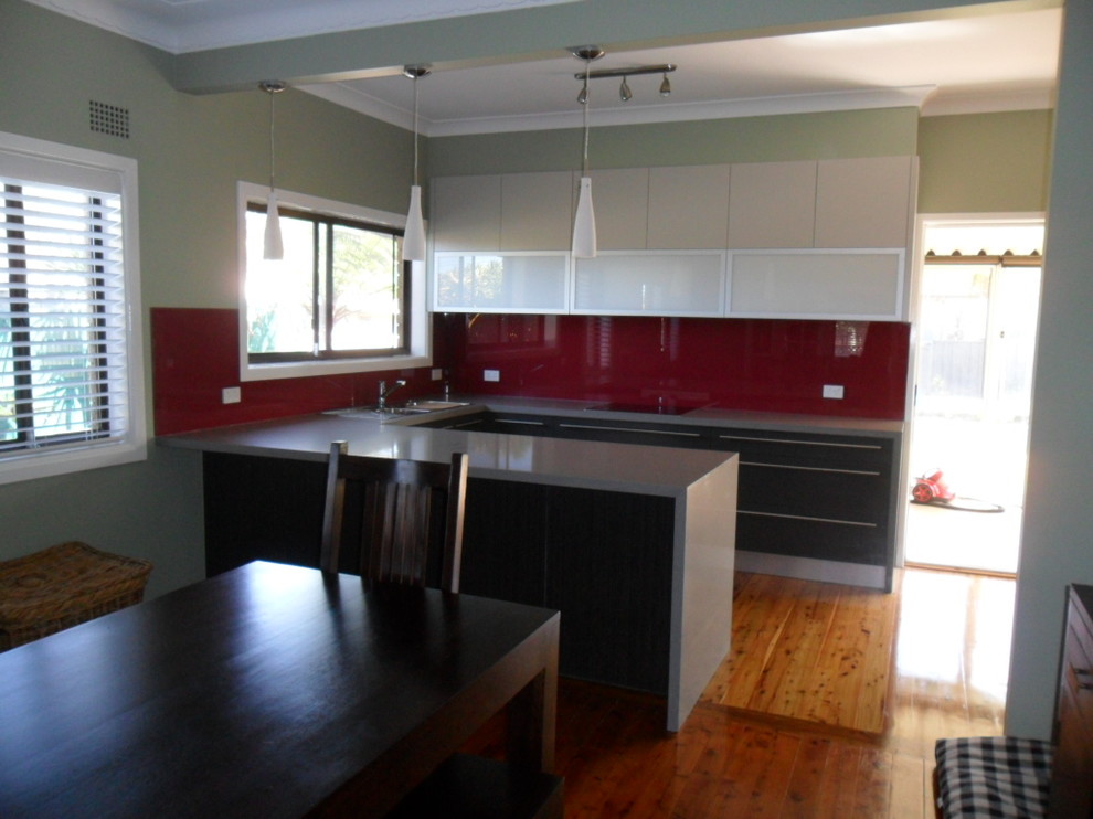Mid-sized modern u-shaped eat-in kitchen in Sydney with a drop-in sink, quartz benchtops, red splashback, glass sheet splashback, stainless steel appliances, light hardwood floors and a peninsula.
