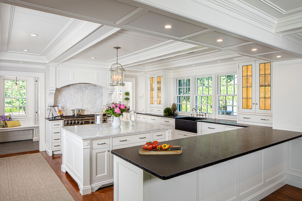 This is an example of a beach style kitchen in Boston with a farmhouse sink, glass-front cabinets, white cabinets, white splashback, marble splashback, stainless steel appliances, medium hardwood floors, with island and orange floor.