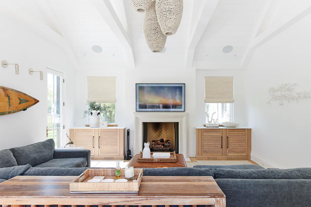 Photo of a beach style living room in New York with white walls, light hardwood floors, a standard fireplace, beige floor and a wall-mounted tv.