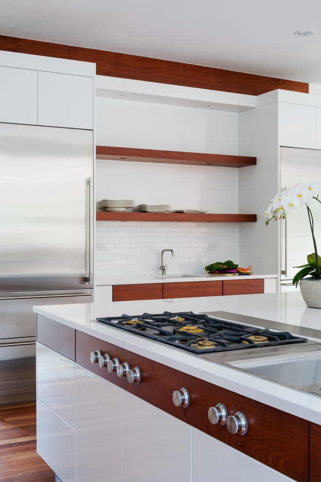 This is an example of an expansive contemporary u-shaped kitchen pantry in Boston with flat-panel cabinets, white cabinets, quartz benchtops, white splashback, ceramic splashback, stainless steel appliances, medium hardwood floors, with island and a double-bowl sink.