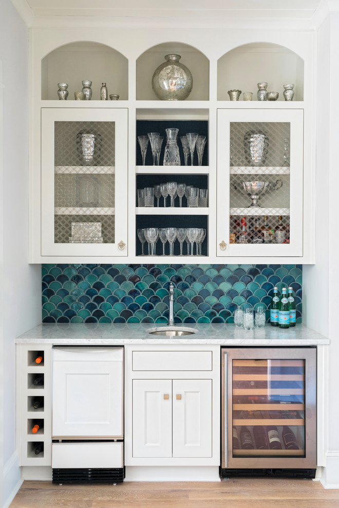 This is an example of a small transitional single-wall wet bar in Atlanta with an undermount sink, recessed-panel cabinets, white cabinets, blue splashback, ceramic splashback, light hardwood floors and brown floor.