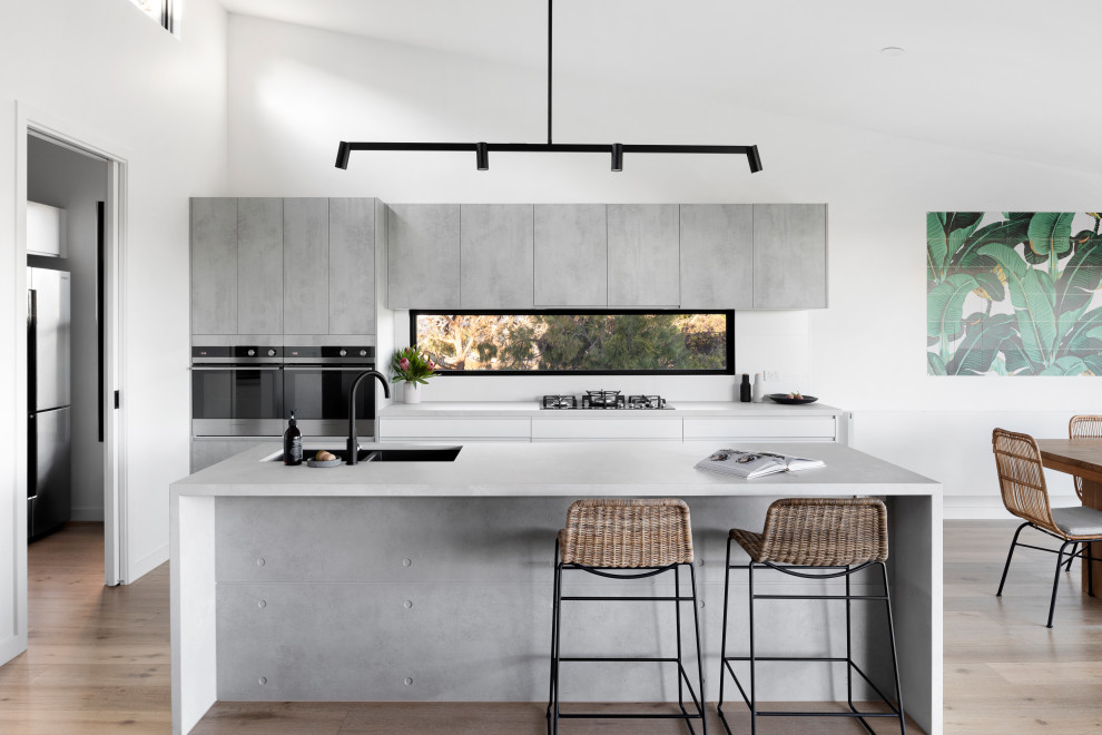 Inspiration for a large contemporary galley open plan kitchen in Melbourne with an undermount sink, flat-panel cabinets, grey cabinets, quartz benchtops, stainless steel appliances, light hardwood floors, with island, beige floor, grey benchtop and window splashback.