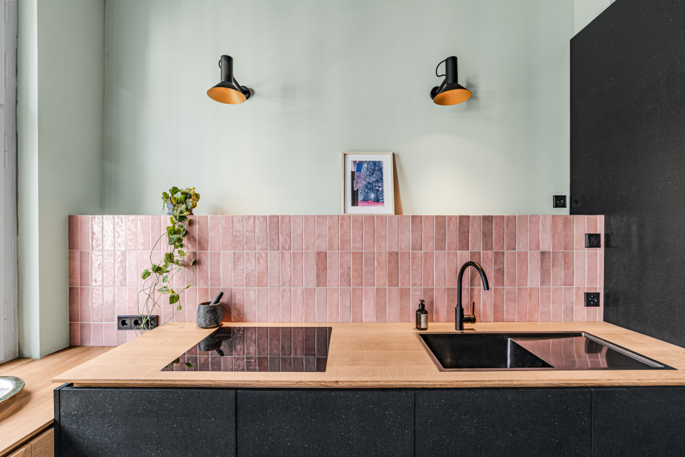 Photo of a mid-sized l-shaped open plan kitchen in Berlin with flat-panel cabinets, black cabinets, wood benchtops, pink splashback, stone tile splashback, dark hardwood floors, no island and green floor.
