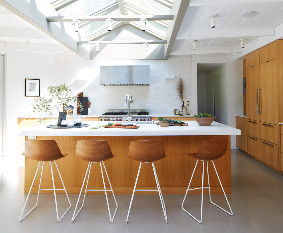 Midcentury kitchen in San Francisco with flat-panel cabinets, medium wood cabinets, white splashback, stainless steel appliances, concrete floors, with island, grey floor and white benchtop.