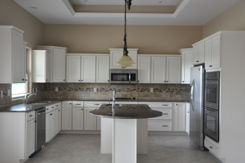 Mid-sized elegant l-shaped travertine floor and beige floor enclosed kitchen photo with a double-bowl sink, recessed-panel cabinets, white cabinets, granite countertops, beige backsplash, stone tile backsplash, stainless steel appliances and an island