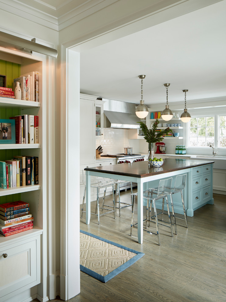 Transitional l-shaped dark wood floor kitchen photo in Chicago with a farmhouse sink, recessed-panel cabinets, blue cabinets, white backsplash, subway tile backsplash, paneled appliances and an island