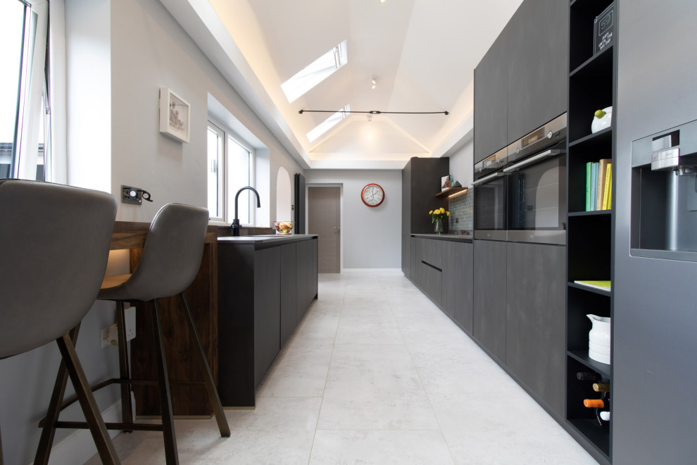 Inspiration for a mid-sized modern galley separate kitchen in Cardiff with an integrated sink, flat-panel cabinets, black cabinets, quartz benchtops, blue splashback, glass tile splashback, black appliances, porcelain floors, no island, white floor and multi-coloured benchtop.