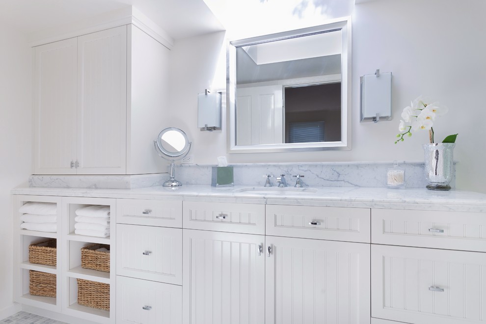 This is an example of a mid-sized beach style master bathroom in Santa Barbara with an undermount sink, beaded inset cabinets, white cabinets, marble benchtops, a one-piece toilet, white tile, stone tile, white walls and mosaic tile floors.